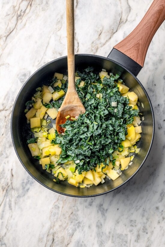 This Prosciutto Wrapped Stuffed Turkey Tenderloin recipe is filled with apples, cheese and kale for a healthy high-protein dinner. Delicious! Kale added to pan of leeks and apples.