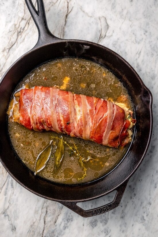 This Prosciutto Wrapped Stuffed Turkey Tenderloin recipe is filled with apples, cheese and kale for a healthy high-protein dinner. Delicious! Skillet with prosciutto-wrapped stuffed turkey tenderloin and broth.