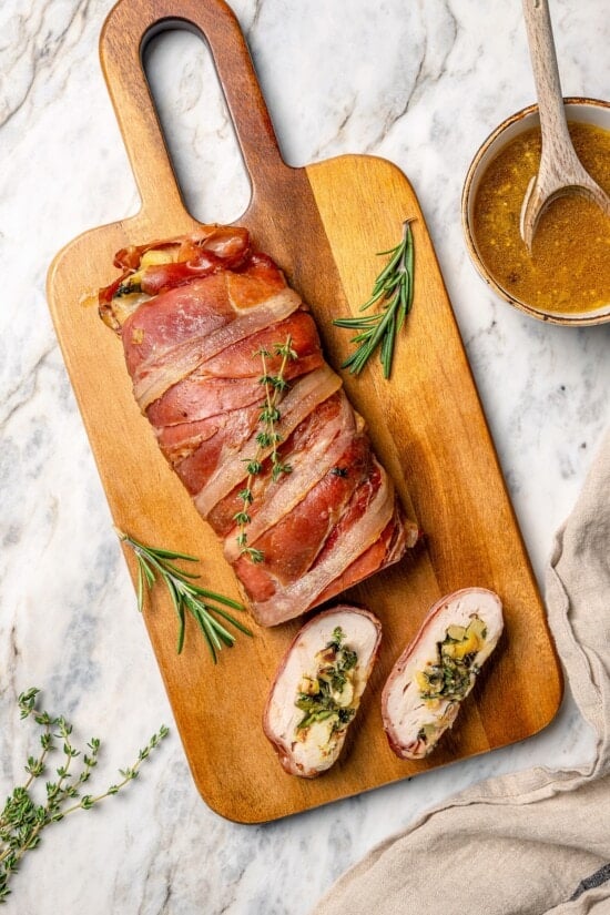 This Prosciutto Wrapped Stuffed Turkey Tenderloin recipe is filled with apples, cheese and kale for a healthy high-protein dinner. Delicious! Two slices of prosciutto-wrapped stuffed turkey tenderloin next to remaining tenderloin.