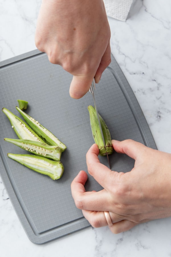 Slicing okra pod in half lengthwise with a small paring knife.