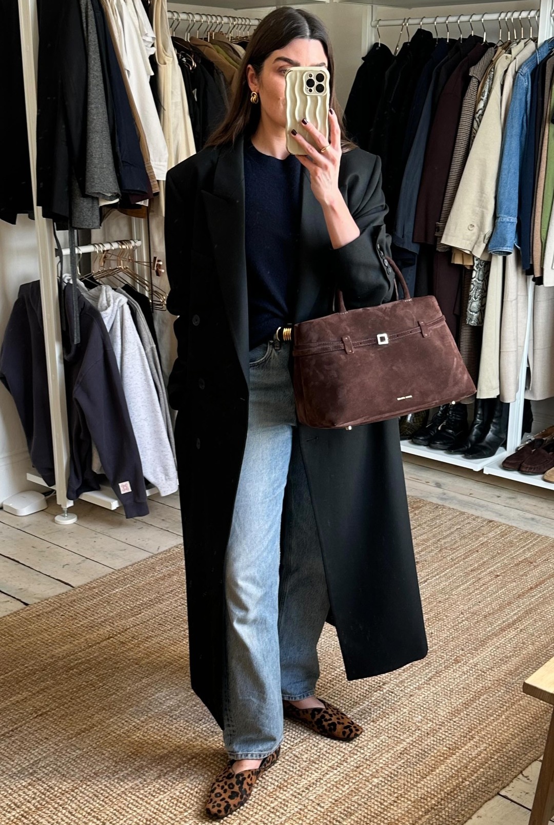 British style influencer Anna Howard poses for. mirror selfie wearing. long black coat, navy blue crewneck sweater, brown suede Manu Atelier bag, straight-leg jeans, and leopard-print v-cut flats