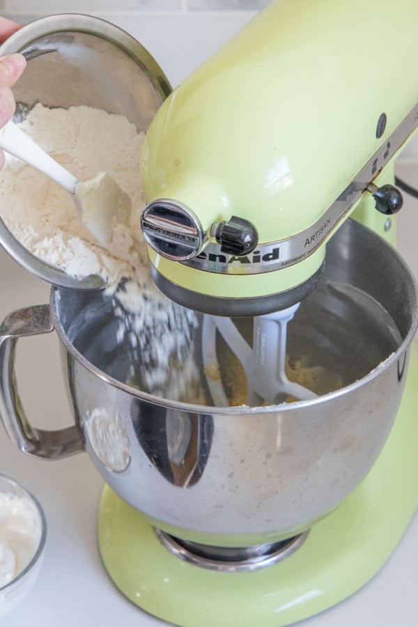 Adding half of dry ingredients to the mixing bowl of a stand mixer.