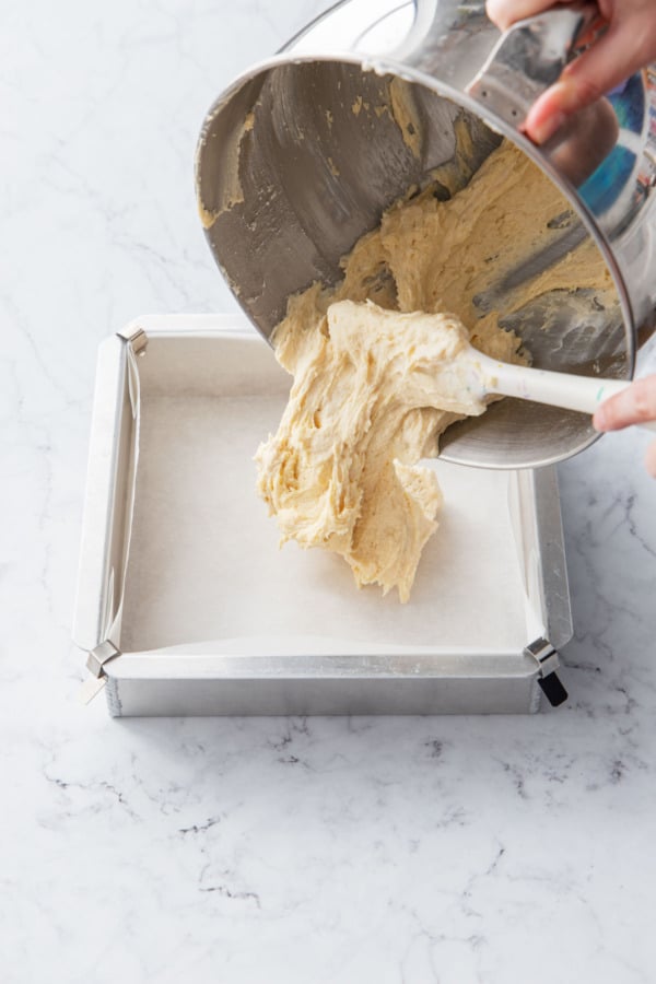 Pouring cake batter into a square cake pan lined with parchment paper.