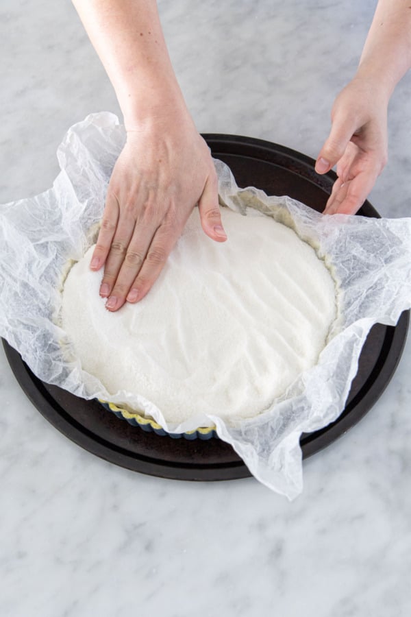 Lining a chilled tart crust with crinkled parchment and filled with granulated sugar for pie weight.