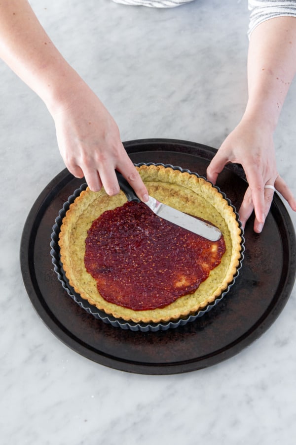 Spreading a layer of raspberry jam into the par-baked tart crust.