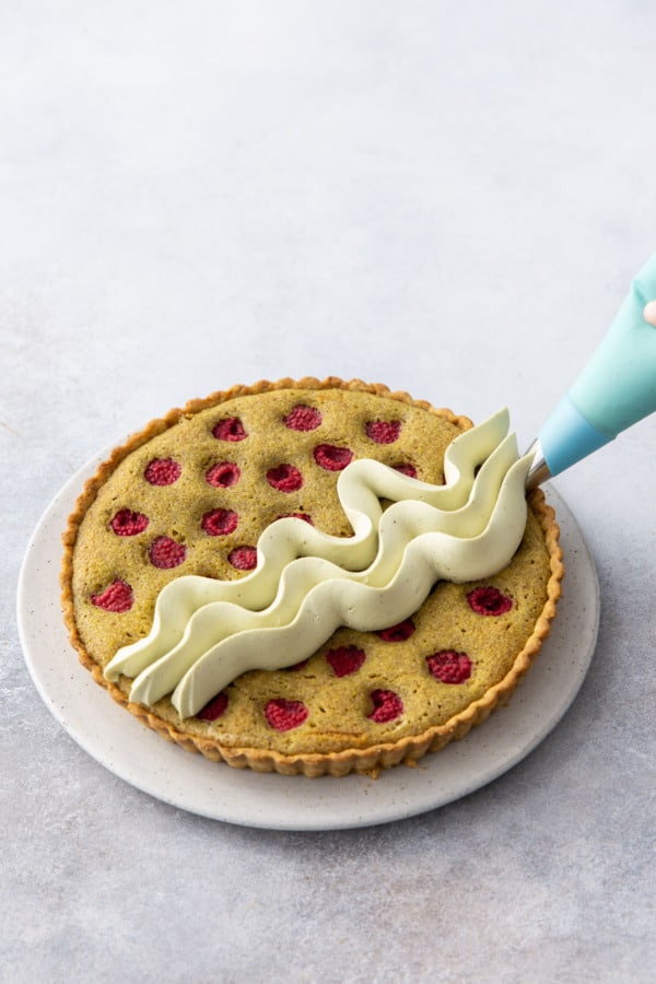 Piping squiggly waves onto top of baked pistachio raspberry frangipane tart using a Saint Honore piping tip.