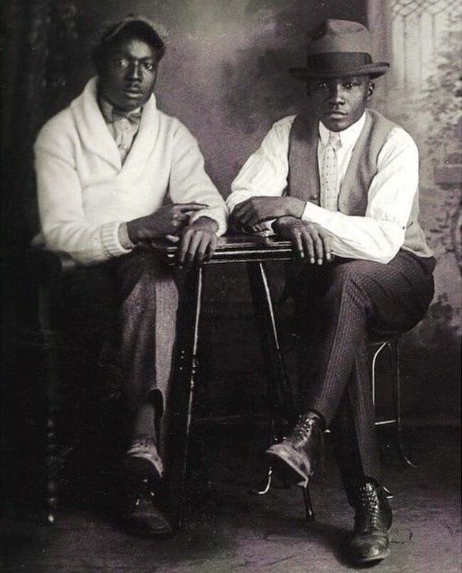 two men in 1920s sitting on a chair with arms resting on a table