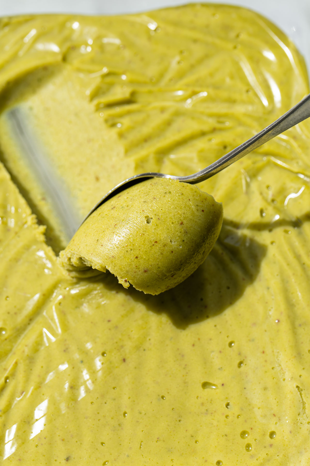 Close up shot of a spoon scooping a curl of bright green pistachio ganache.