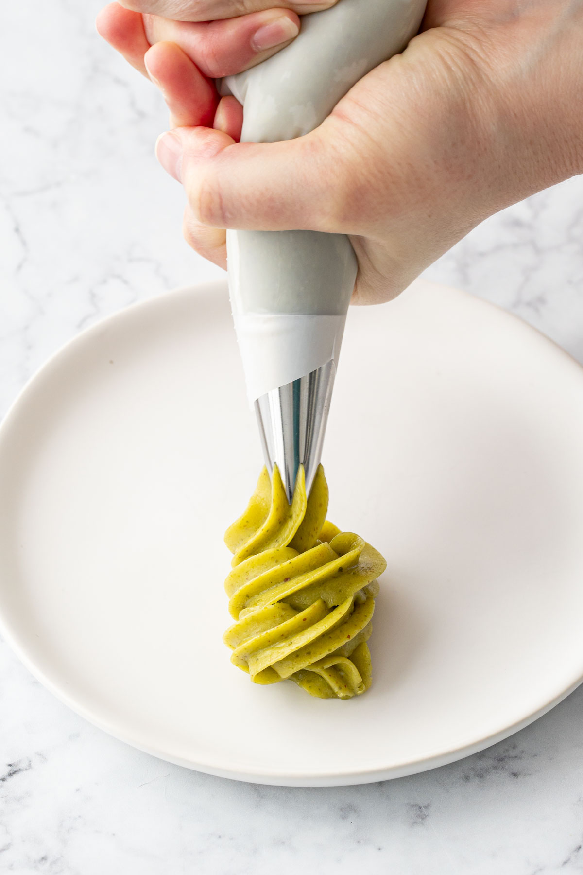 Piping a swirl of bright green pistachio ganache onto a white plate.