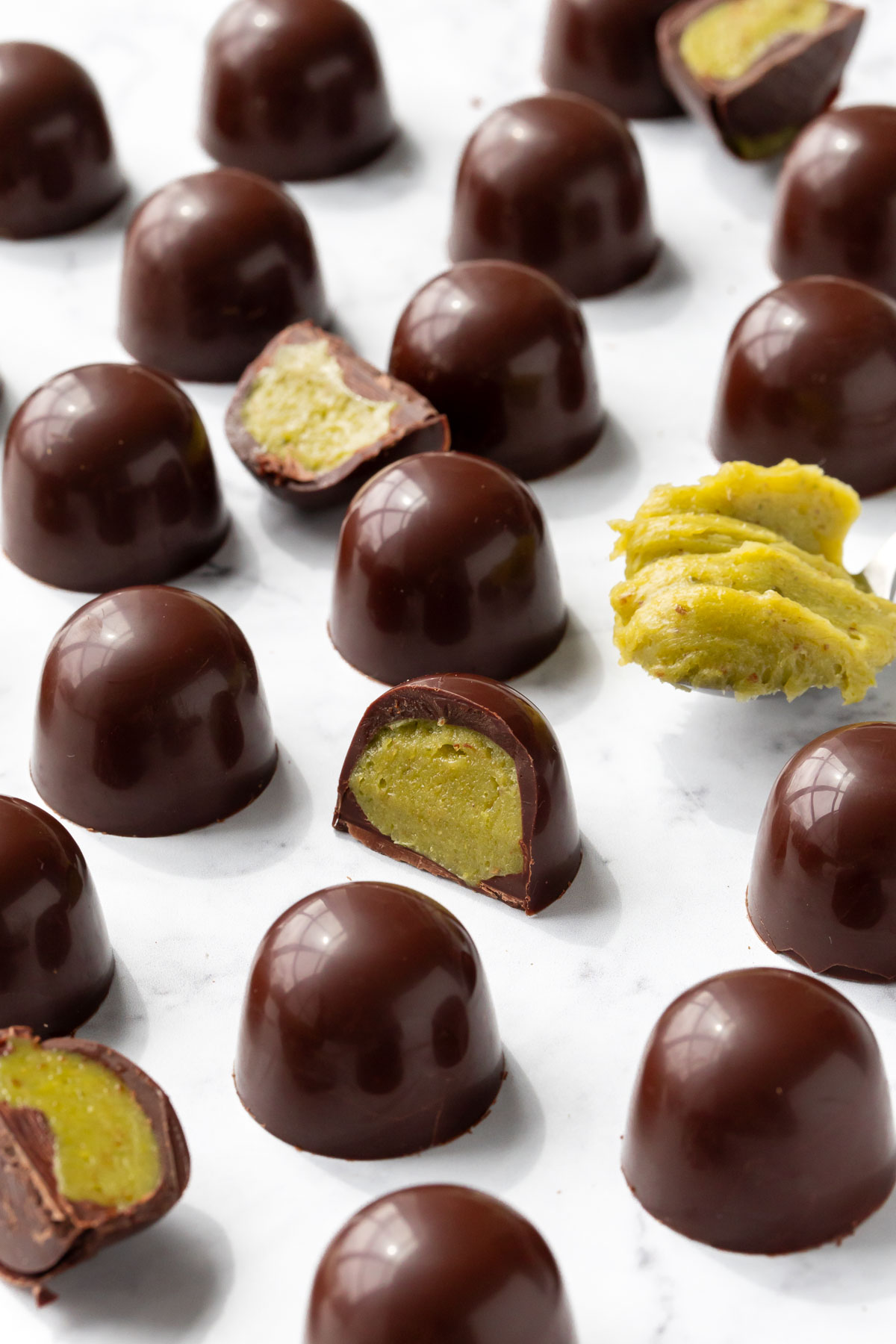 Dark chocolate truffles on a marble surface, a few cut in half to show the bright green homemade pistachio ganache inside.
