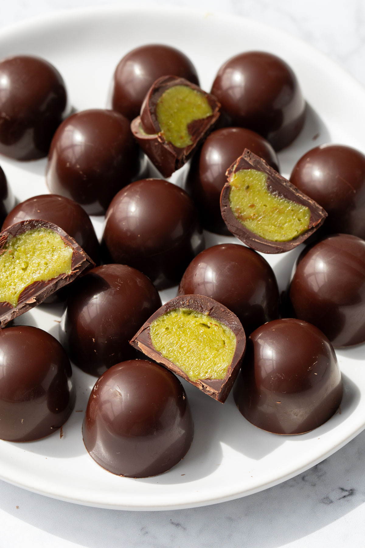 Plate piled with dark chocolate truffles, a few cut in half to show the bright green homemade pistachio ganache inside.