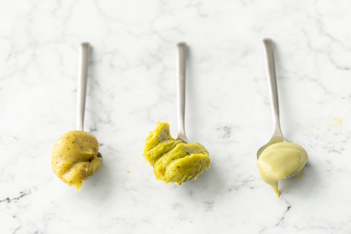 Three spoons comparing the color and appearance of storebought pistachio butter, homemade, and pistachio cream.
