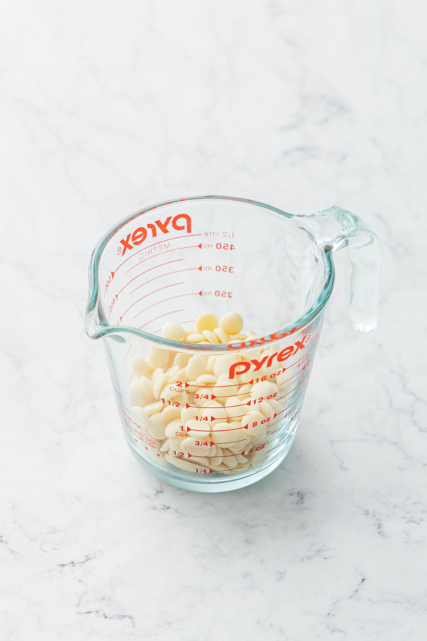 Glass measuring cup with white chocolate callets ready to be melted.