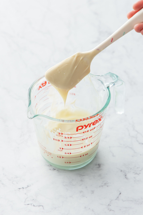 Spatula with melted white chocolate in a 2-cup glass measuring cup.