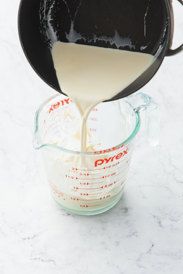 Pouring warmed cream into a glass measuring cup along with melted white chocolate.