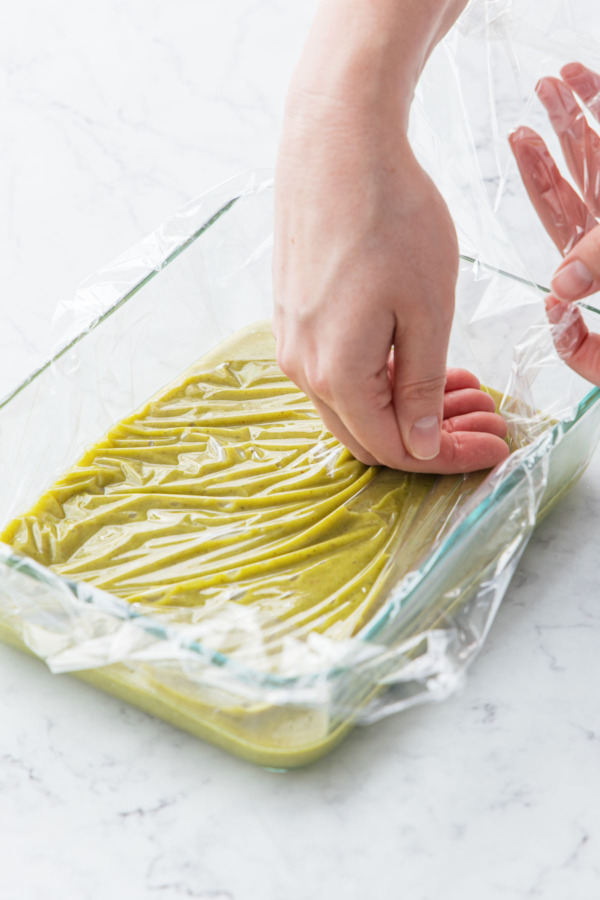 Pressing plastic wrap onto the surface of the pistachio ganache.