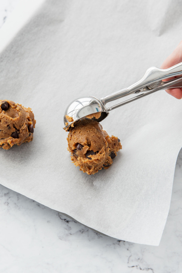 Dropping dough ball onto a parchment lined baking sheet.