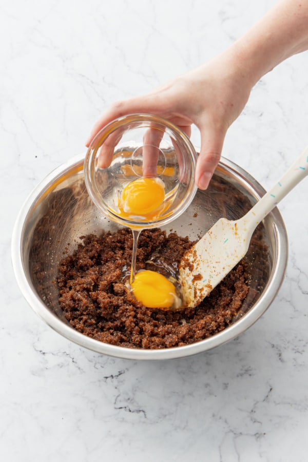 Adding one egg and one egg yolk to mixing bowl with butter and sugars.