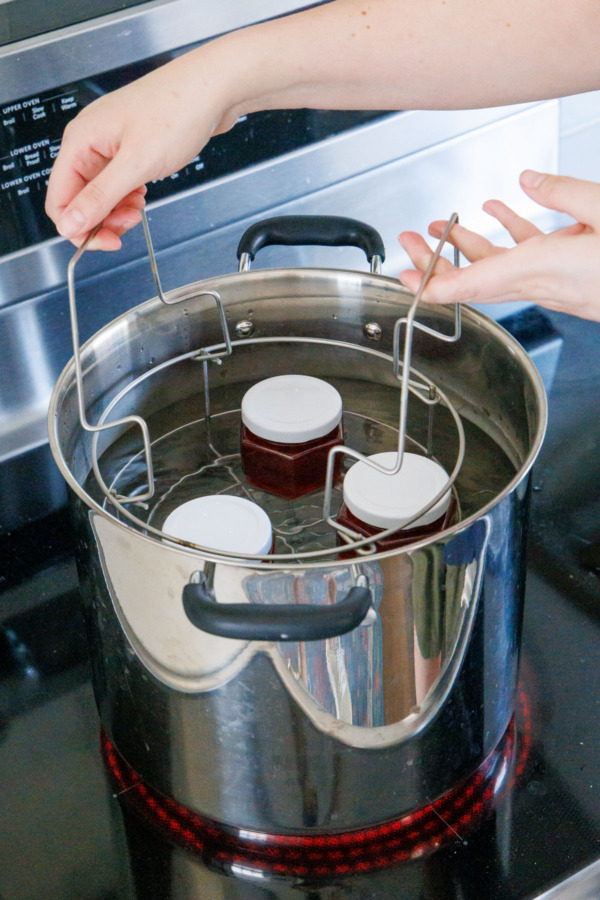 Submerging jelly jars into a boiling water bath in a large stockpot full of water.