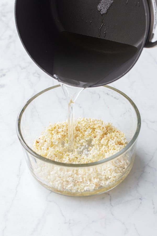 Pouring warm simple syrup over the fresh elderflowers in a heat-proof glass container.