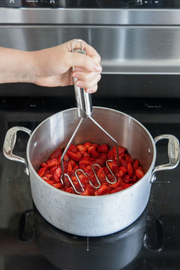 Mashing chopped strawberries in a saucepan.
