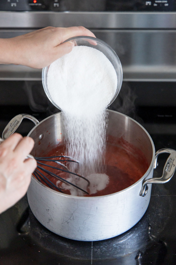 Adding sugar to boiling strawberry mixture.