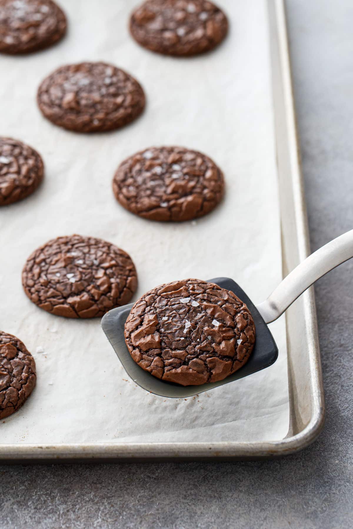 Chewy Crinkle-Top Brownie Cookies on a cookie sheet, spatula lifting up one of the cookies.
