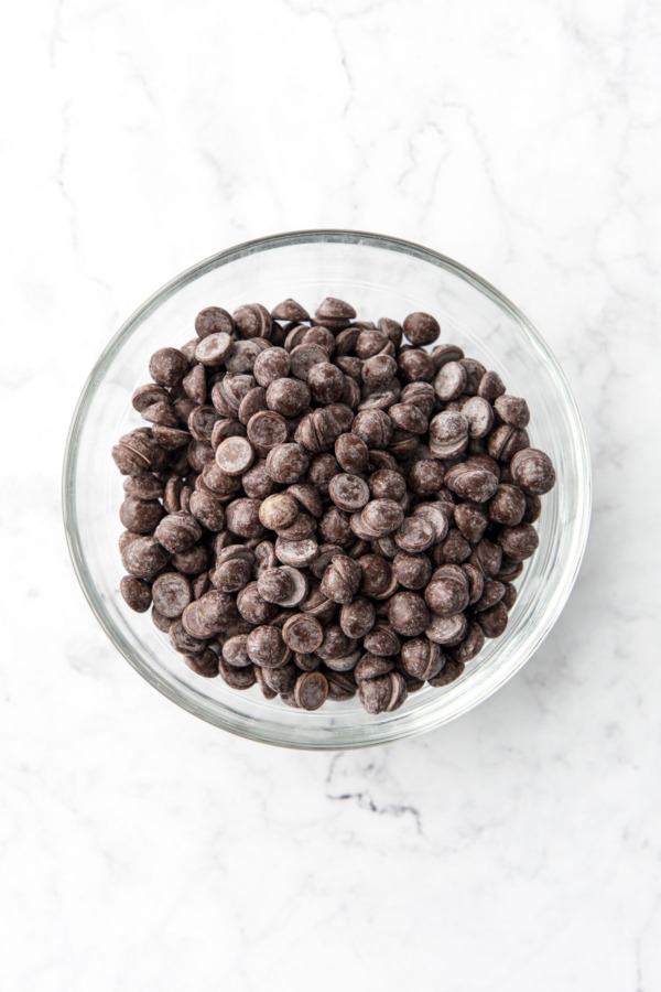 Bowl of semisweet chocolate callets on a white marble background.