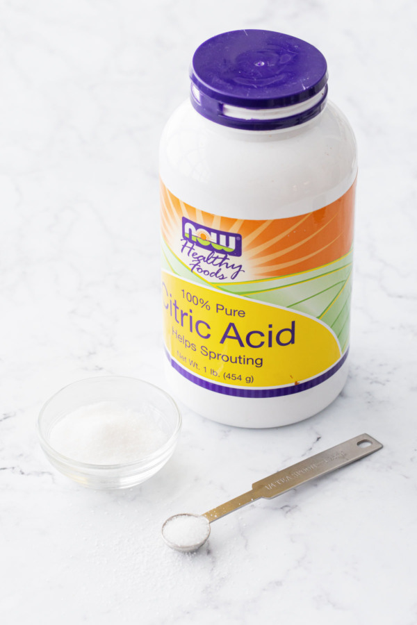 Bottle of citric acid with a small bowl and measuring spoon on the side.