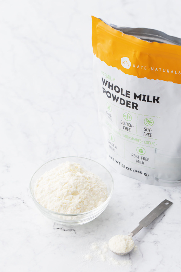Bag of dry milk powder showing packaging, plus a bowl and spoonful of milk powder on the side.