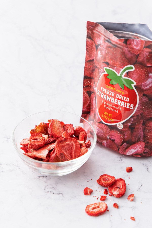 Bag of freeze-dried strawberries with a bowl full and a few pieces scattered on the side.