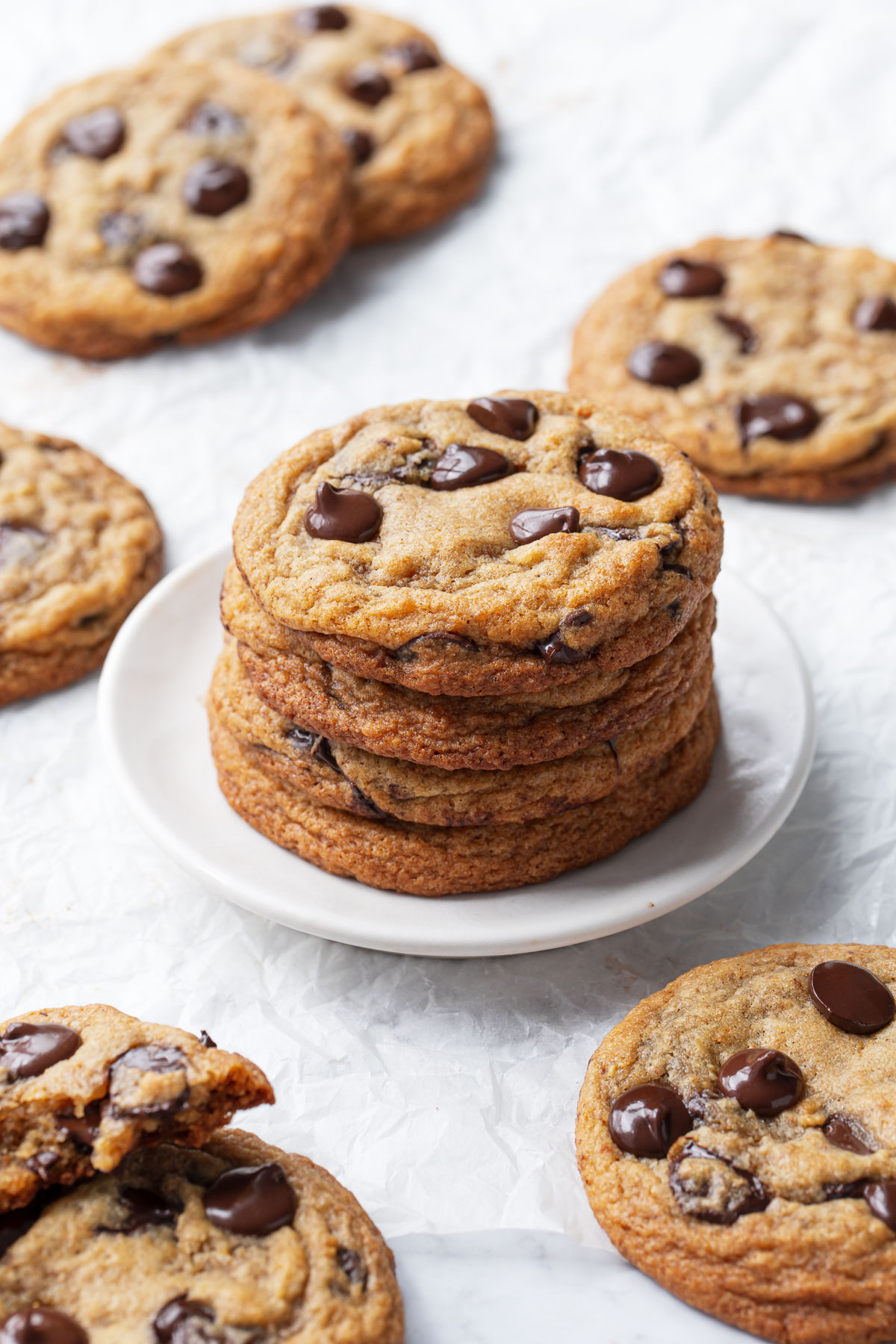 Stack of Brown Butter Banana Bread Chocolate Chip Cookies on a white plate, more cookies scattered in the background.