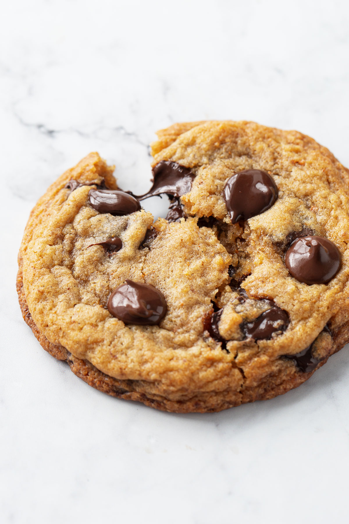 Brown Butter Banana Bread Chocolate Chip Cookie broken in half with threads of melted chocolate chips stretching in between.