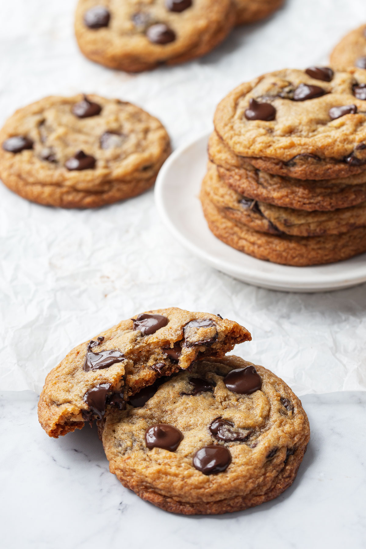 Brown Butter Banana Bread Chocolate Chip Cookies, one cookie broken in half to show interior texture, with a stack of cookies in the background.