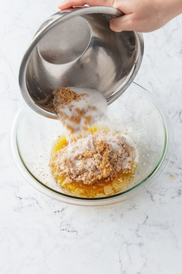 Adding sugar and brown sugar to brown butter in a glass mixing bowl.
