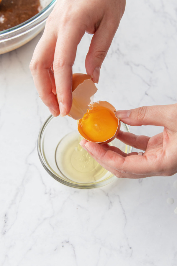 Separating an egg over a small glass ramekin to catch the whites.