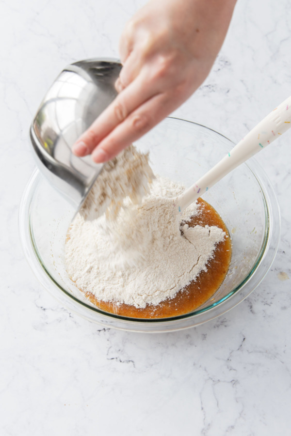 Adding dry ingredients to mixing bowl with wet ingredients.