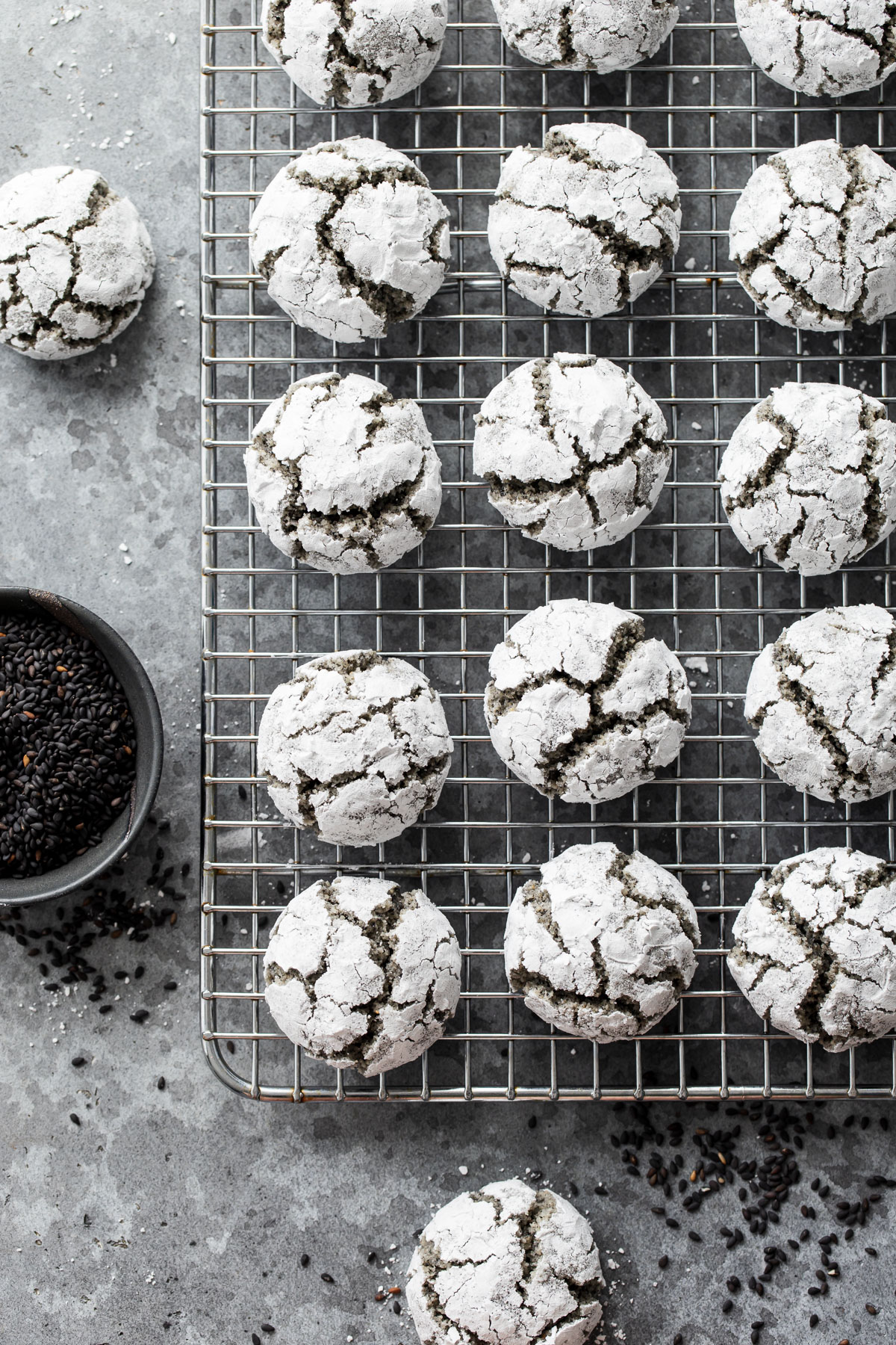 Overhead view of Black Sesame Amaretti Cookies on a wire rack, with a bowl of black sesame seeds on the side.