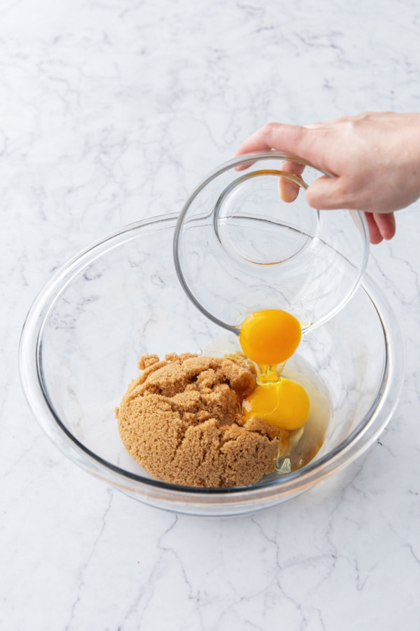 Adding 2 eggs to a glass mixing bowl with brown sugar.