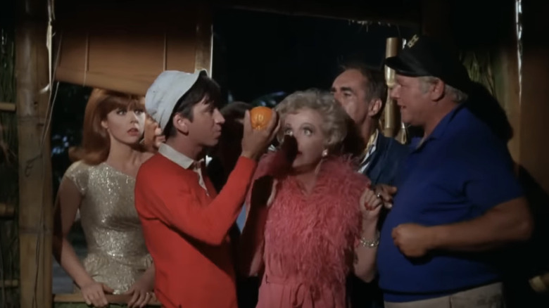 Bob Denver's Gilligan holds up an orange as Jim Backus' Thurston Howell III, Natalie Schafer's Eunice "Lovey" Howell, Tina Louise's Ginger Grant, and Alan Hale Jr's Jonas Grumby watch in Gilligan's Island