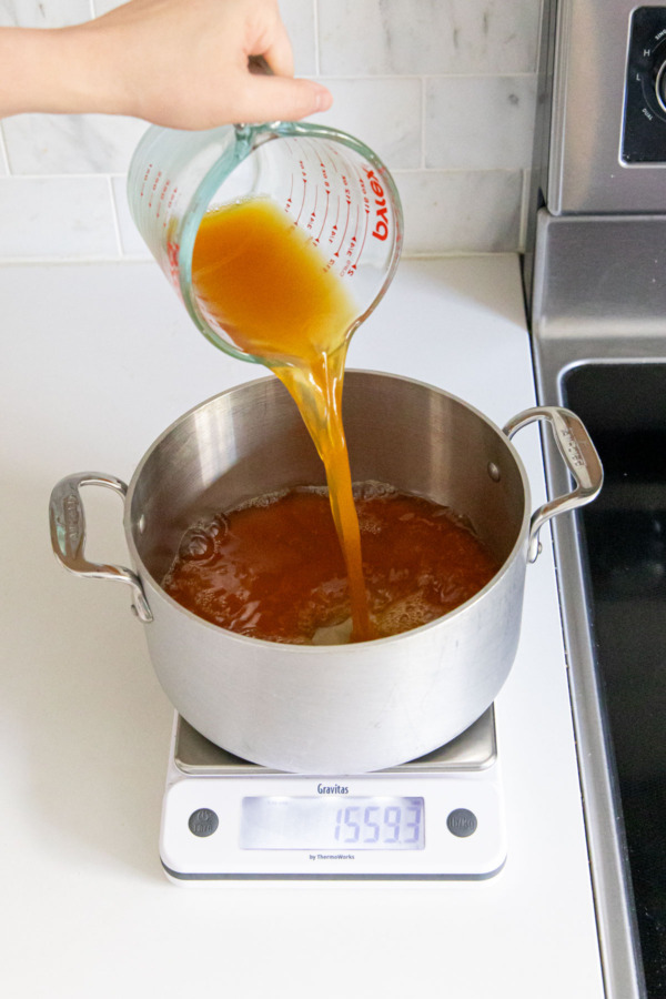 Pouring apple cider into a saucepan set on top of a digital scale.