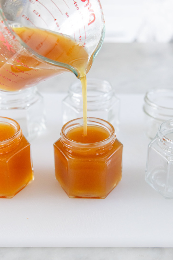 Pouring finished apple cider jelly into glass jelly jars with 1/4-inch headspace.