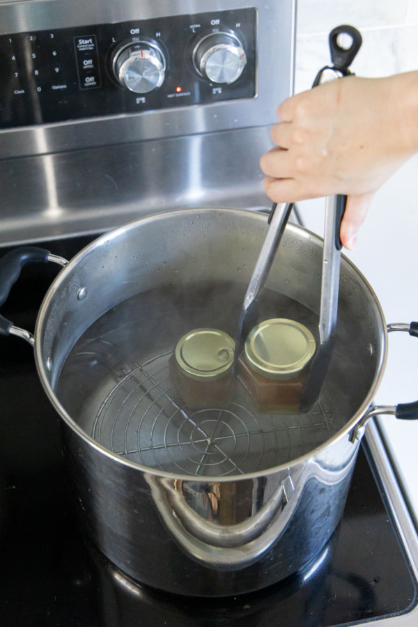 Lowering jars of jelly into a pot filled with boiling water before water-bath processing.